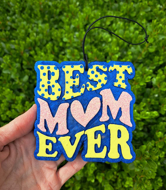 Decorative freshie with 'BEST MOM EVER' text held against a green leafy background