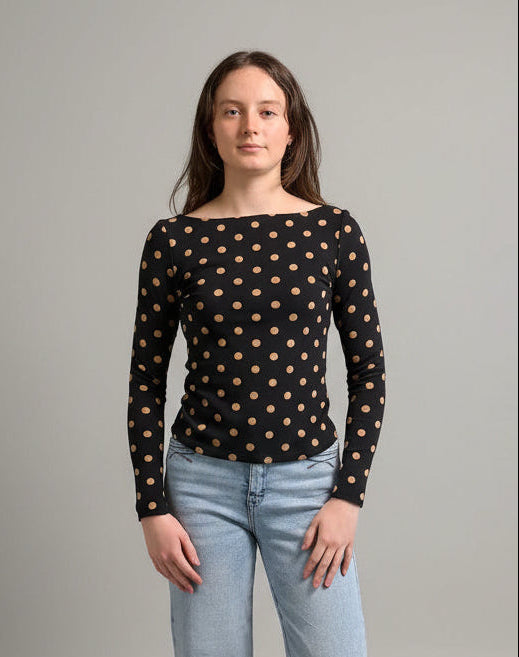 woman wearing a black polka dot long sleeve top with blue jeans against a neutral background