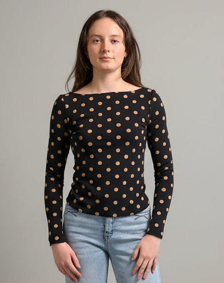 woman wearing a black polka dot long sleeve top with blue jeans against a neutral background