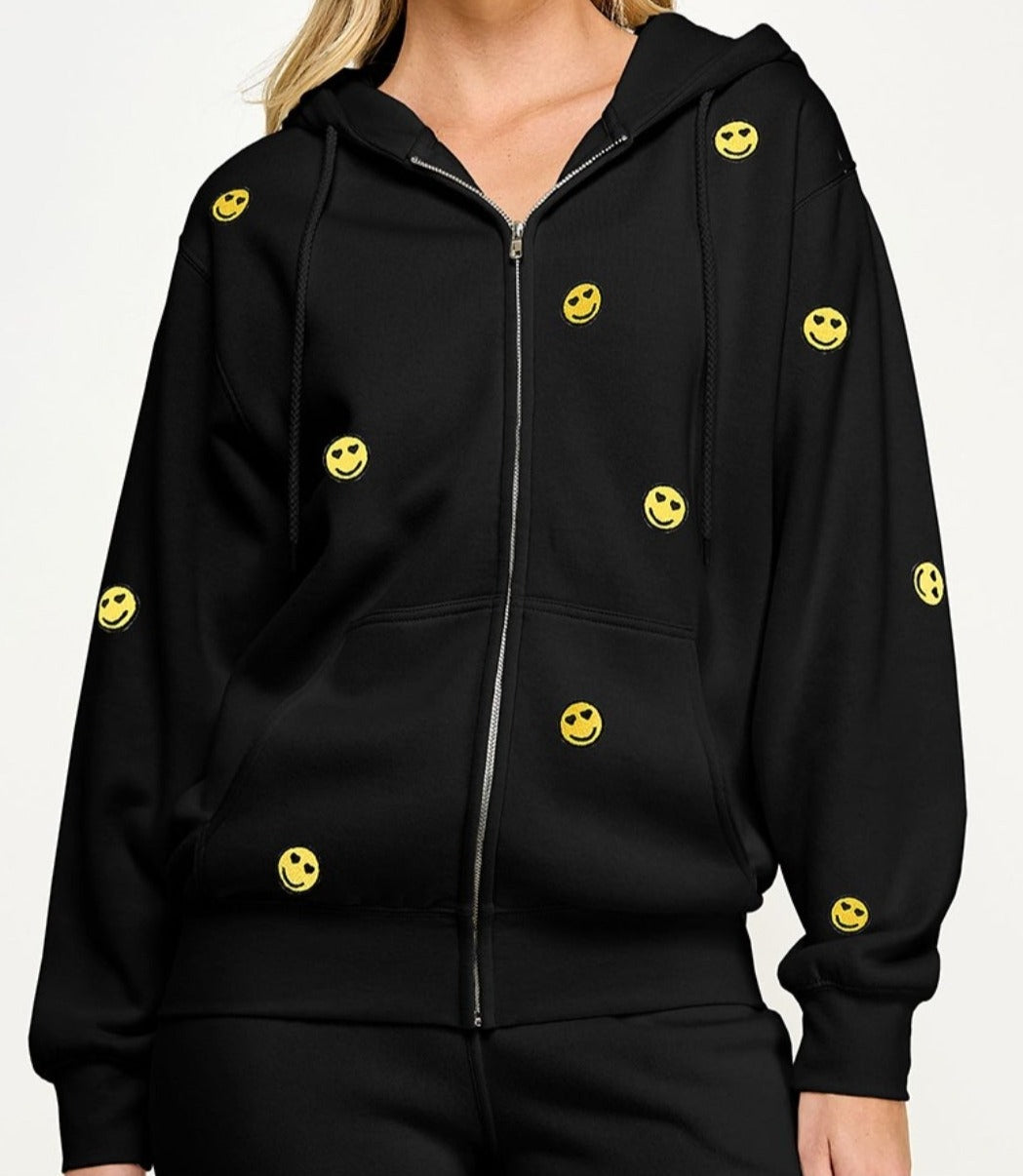A black zip front hoodie with smiley face embroidery, featuring a hood, drawstring, long sleeves, and pockets.
