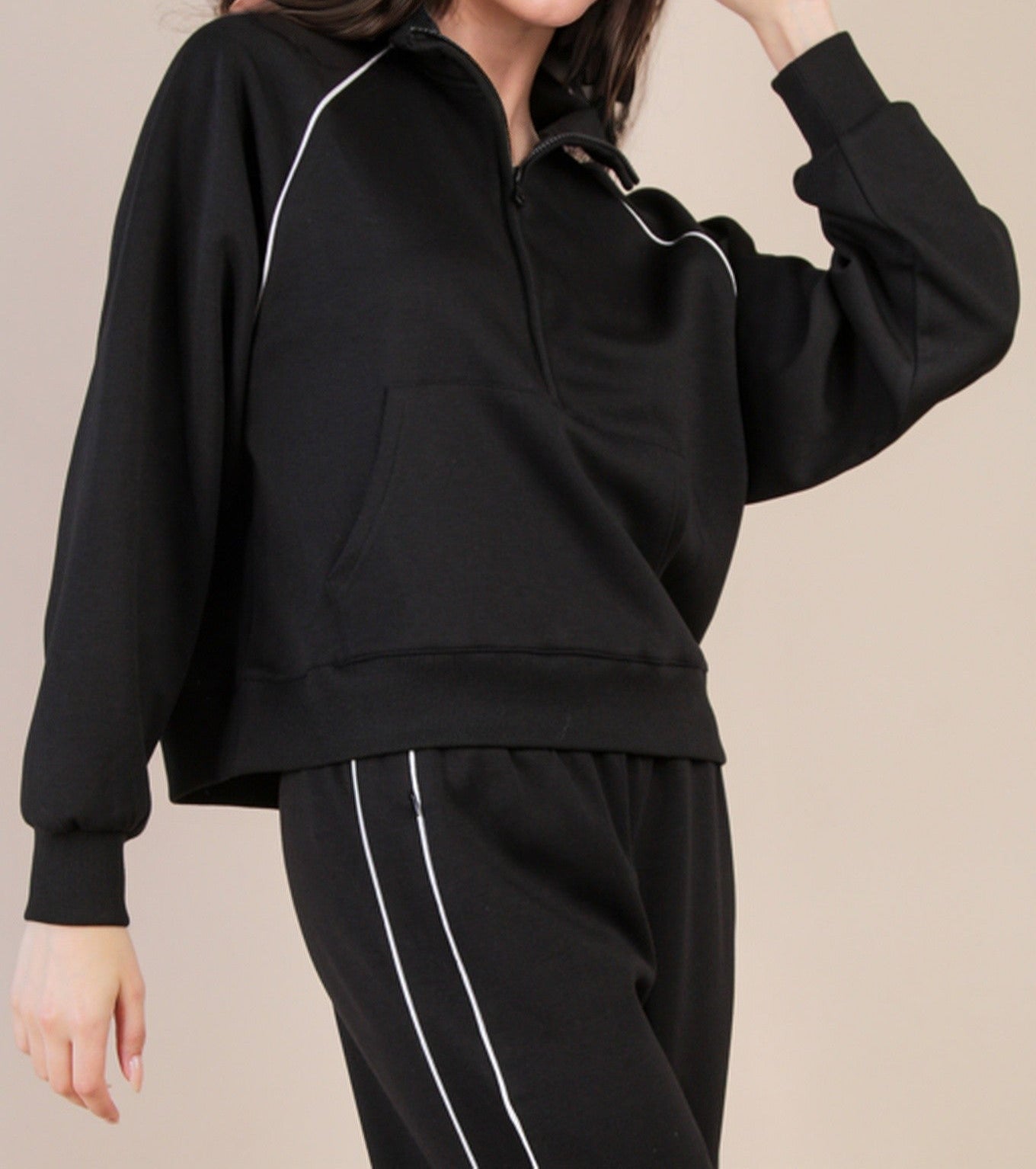 Woman wearing a black tracksuit with white piping on a beige background