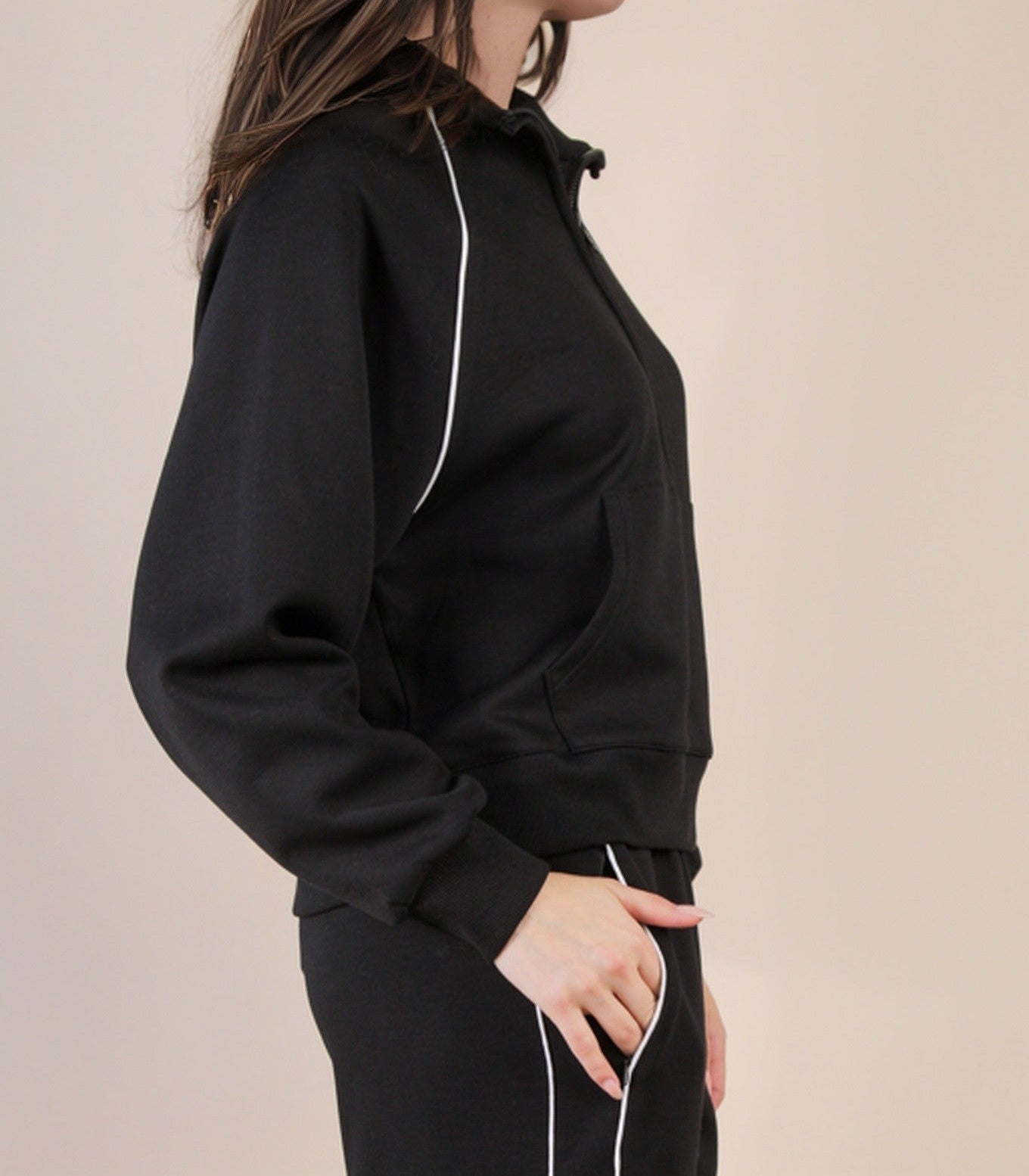 Woman wearing a black outfit with white piping on a beige background