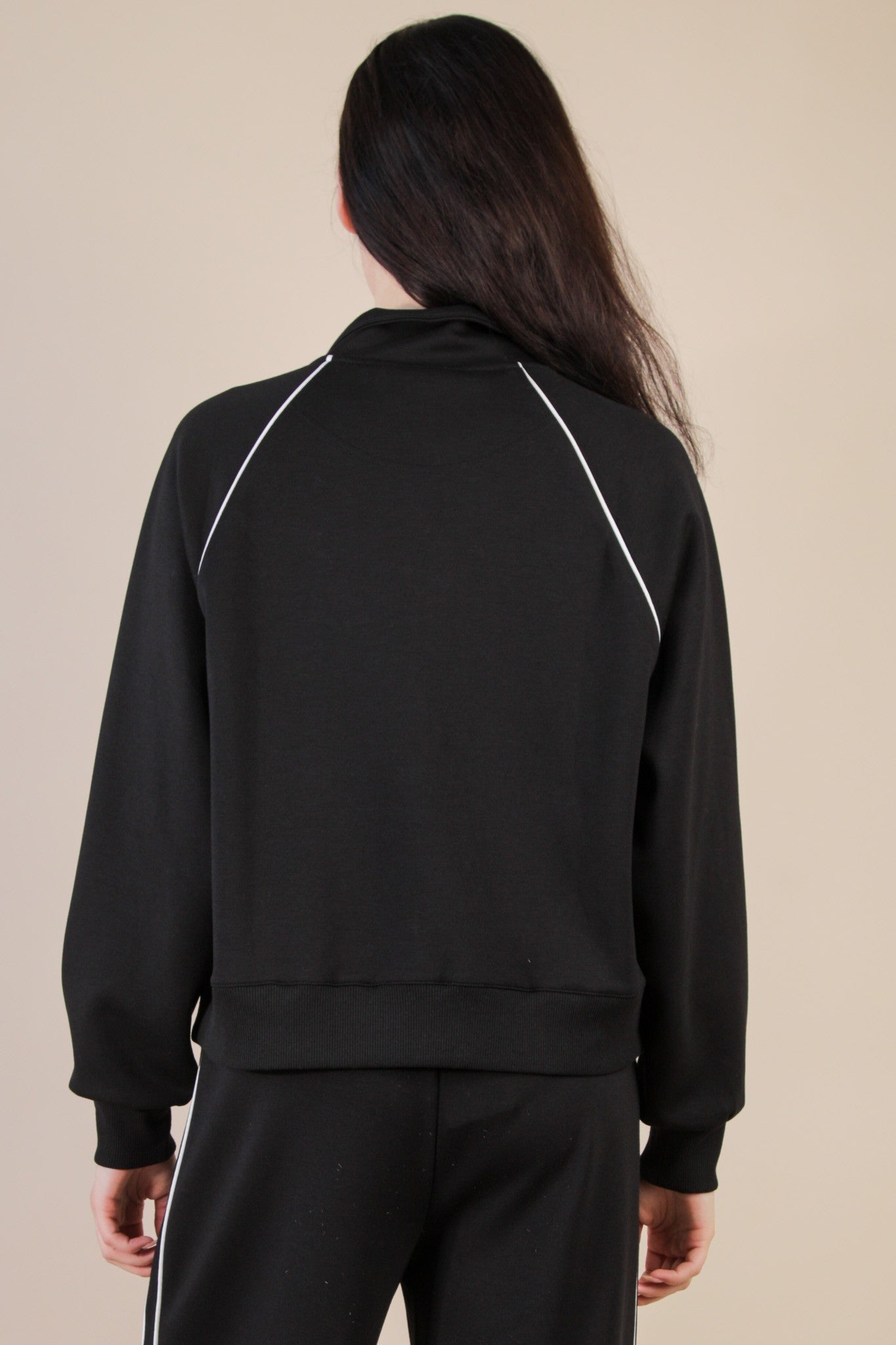 Person wearing a black tracksuit with white piping on a beige background