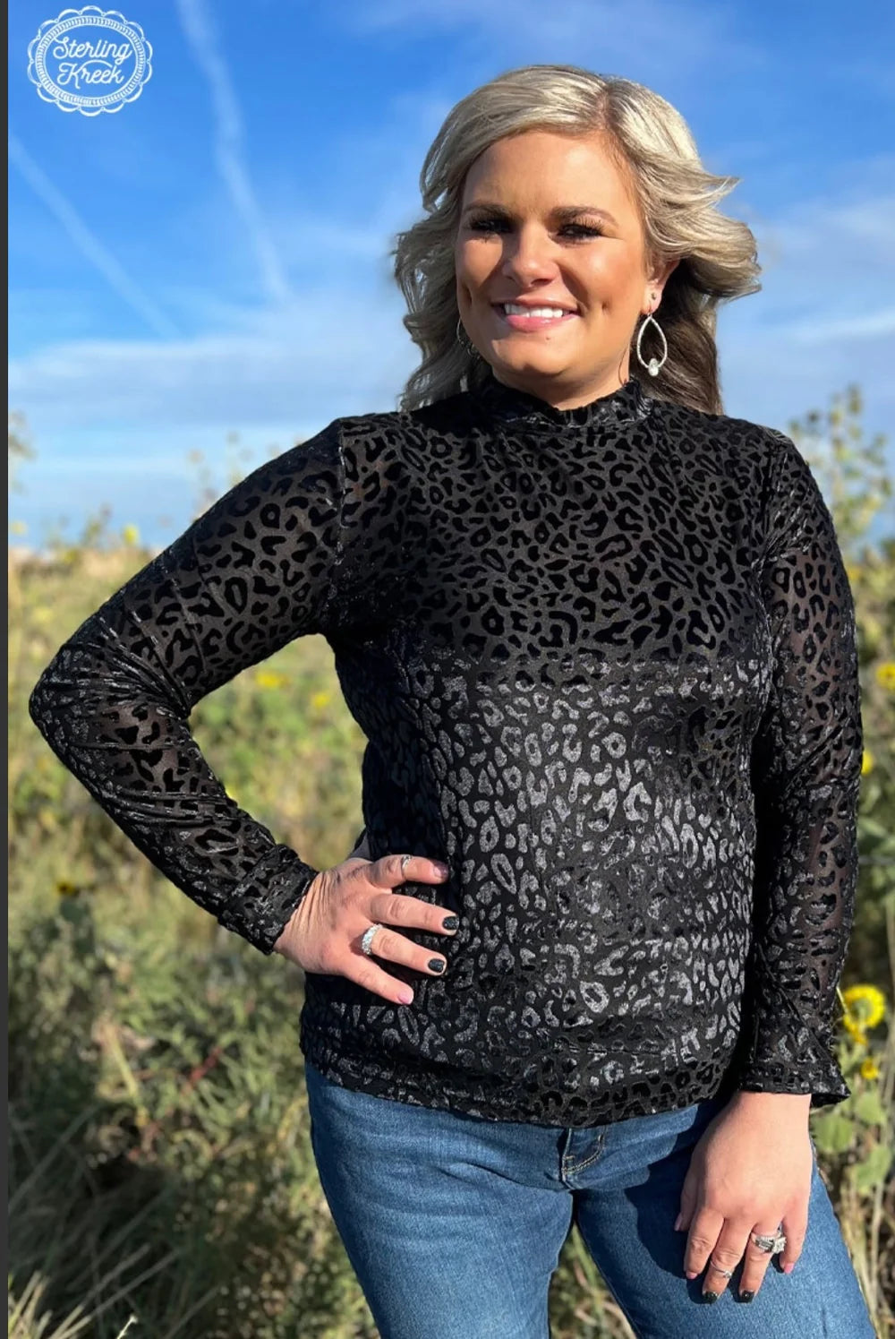 Woman wearing a black leopard print long-sleeve top and blue jeans outdoors.