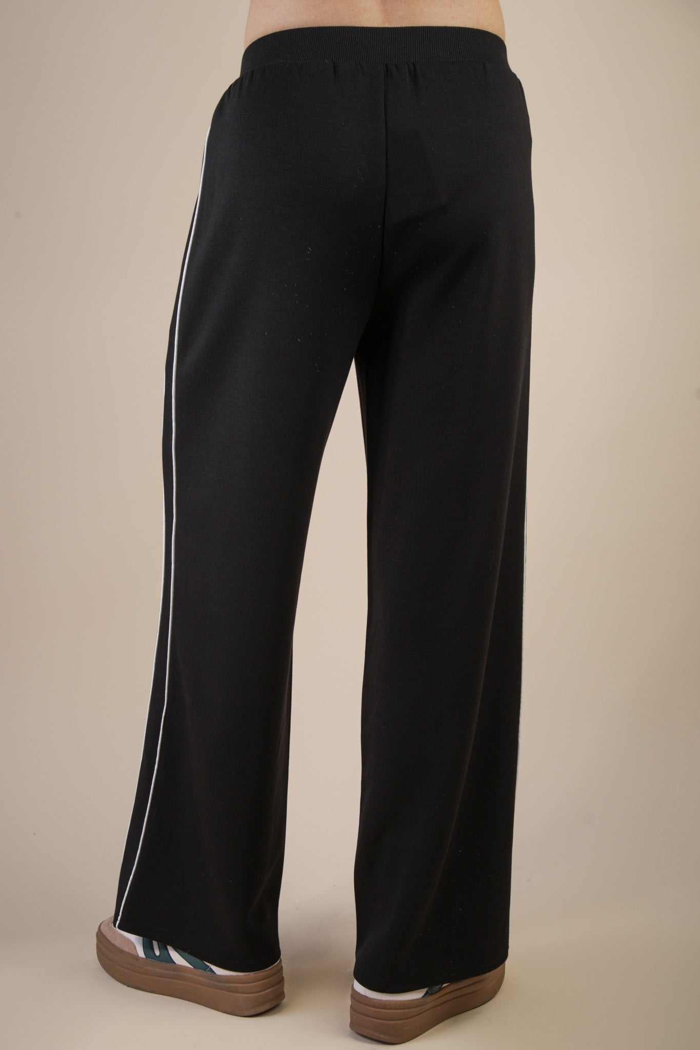 back view of black track pants with white stripes on beige background