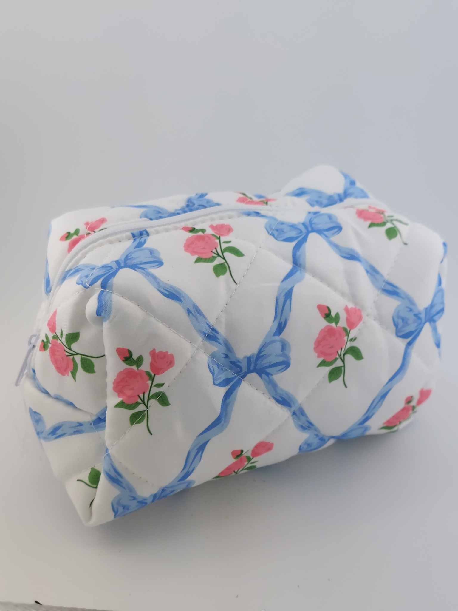 A blue cosmetic makeup pouch with a floral pattern featuring pink flowers and green leaves, with blue ribbons.