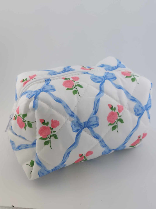 A blue cosmetic makeup pouch with a floral pattern featuring pink flowers and green leaves, with blue ribbons.