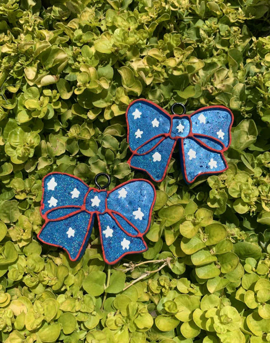 Two blue bow air fresheners with white stars on a green leafy background