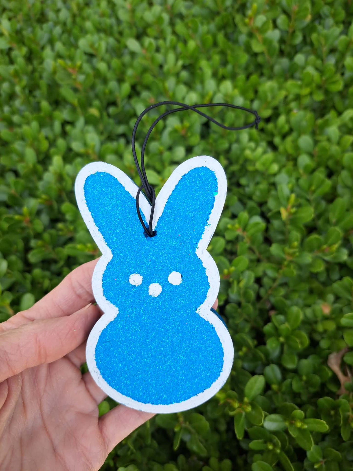 Blue bunny-shaped air freshener held against a green bush background