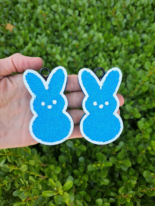 Blue bunny-shaped earrings held in a hand with a green leafy background