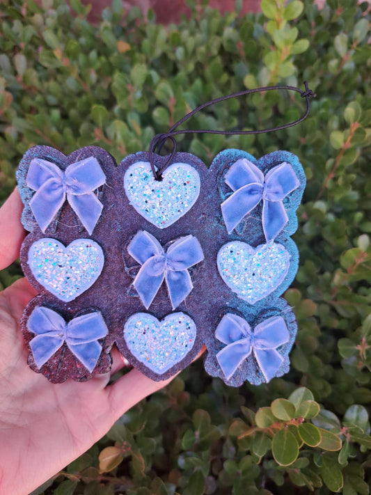 Decorative heart and bow freshie held in front of a green bush