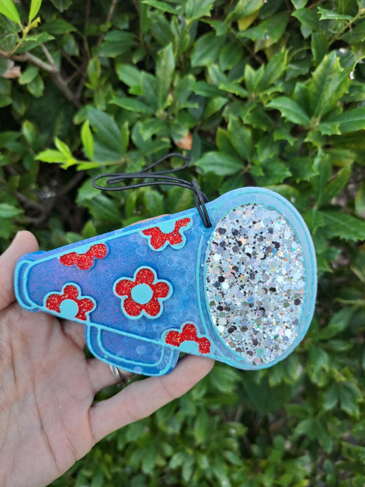 Blue megaphone freshie with red flowers held against a green leafy background