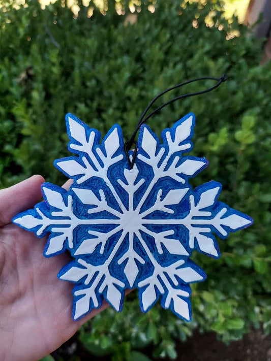 Blue and white snowflake frshie held in front of green foliage