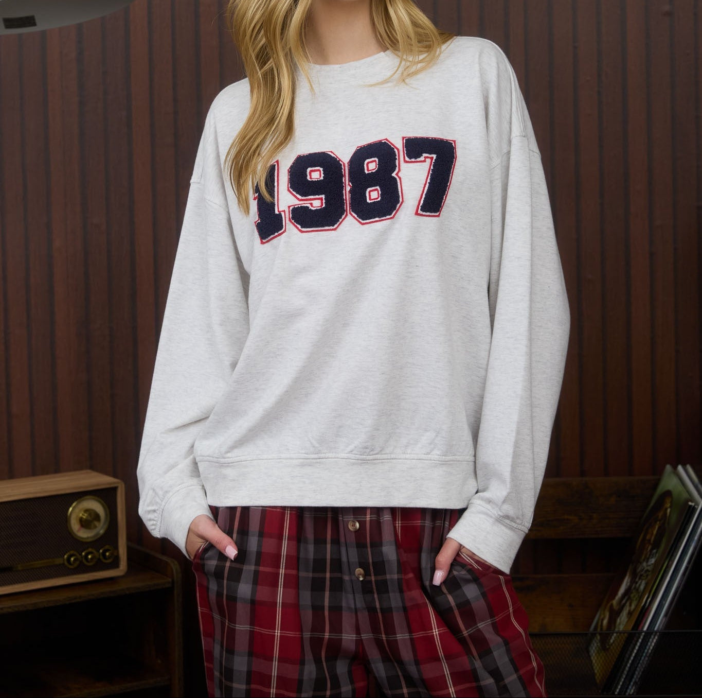 Person wearing a white sweatshirt with '1987' printed on it against a striped wall.