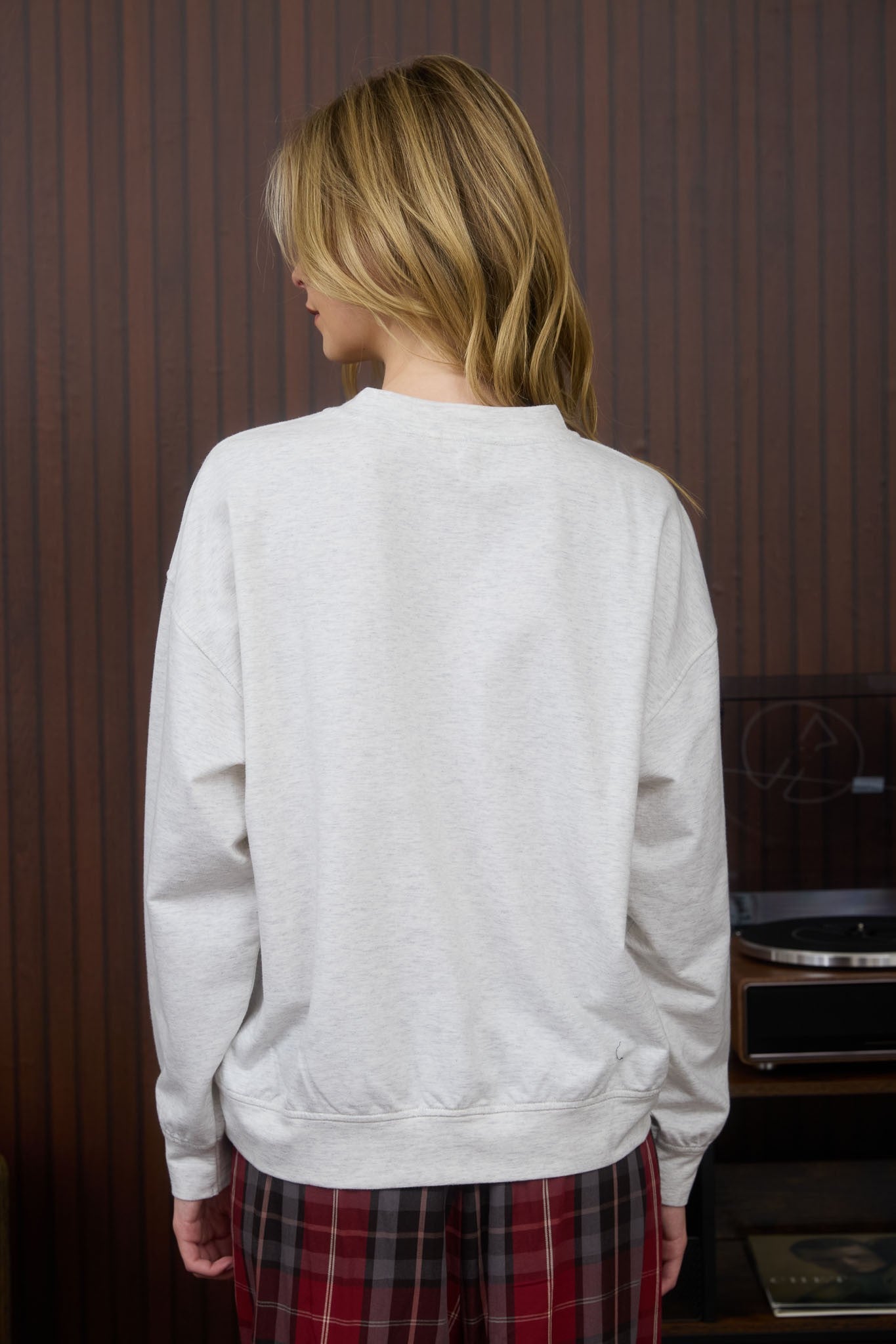 Person wearing a light gray sweatshirt and plaid pants in a room with striped wallpaper.