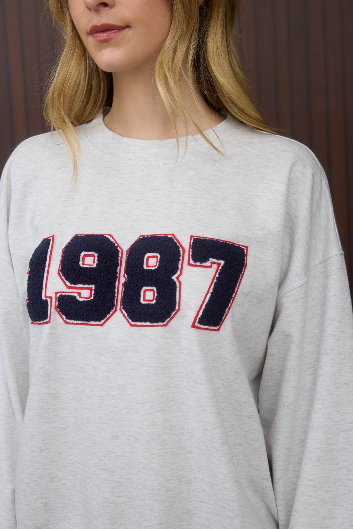 Person wearing a gray sweatshirt with '1987' printed on it against a brown background