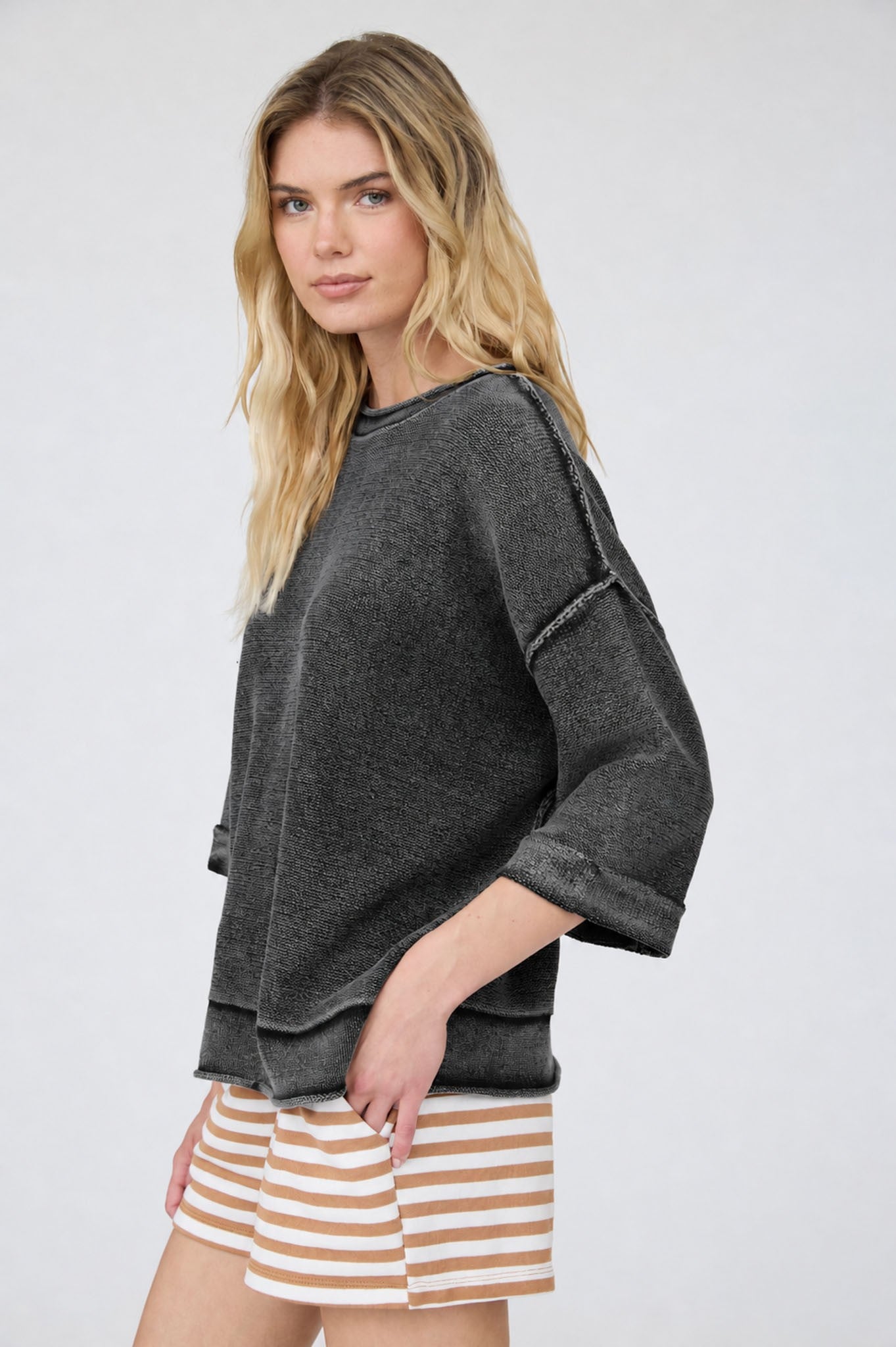 Woman wearing a dark gray oversized sweater and striped shorts on a white background
