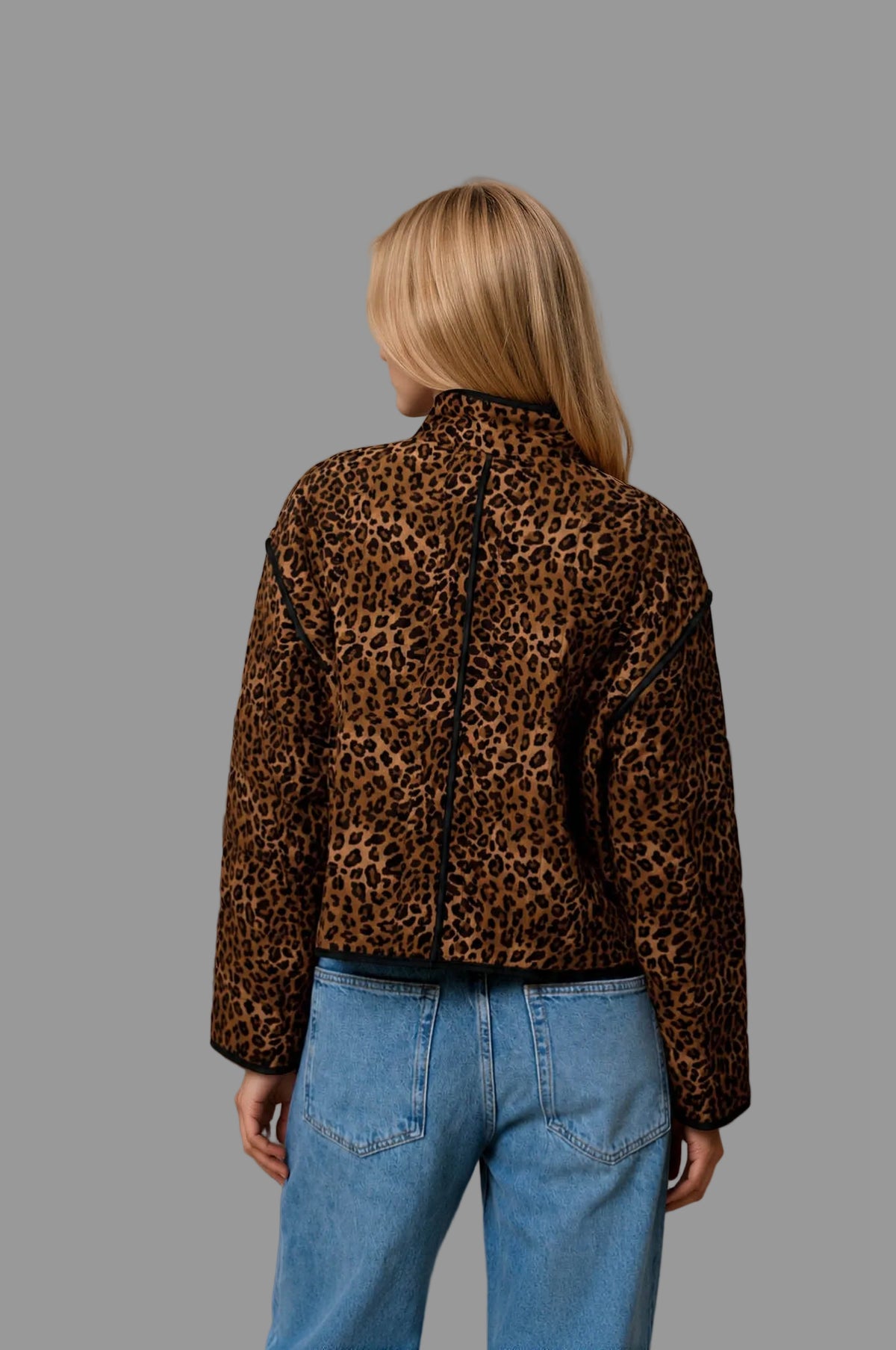back view of a woman wearing a leopard print quilted jacket with jeans against a neutral background.