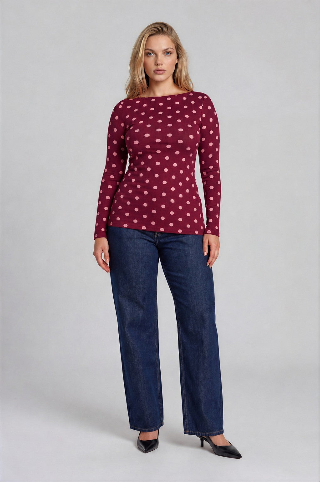 Woman wearing a burgundy polka dot top and blue jeans on a gray background