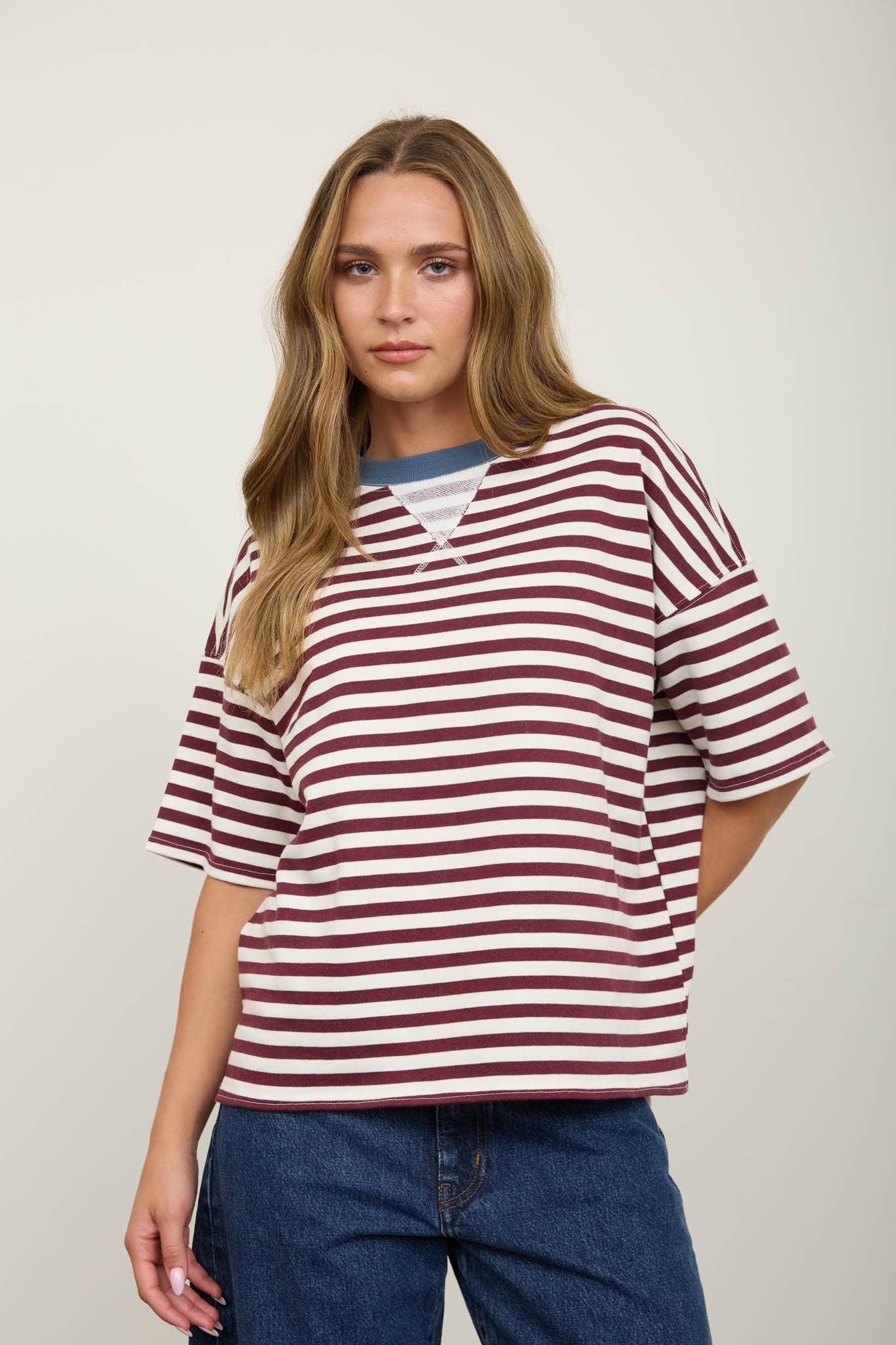 Woman wearing a burgundy striped shirt and jeans against a plain background