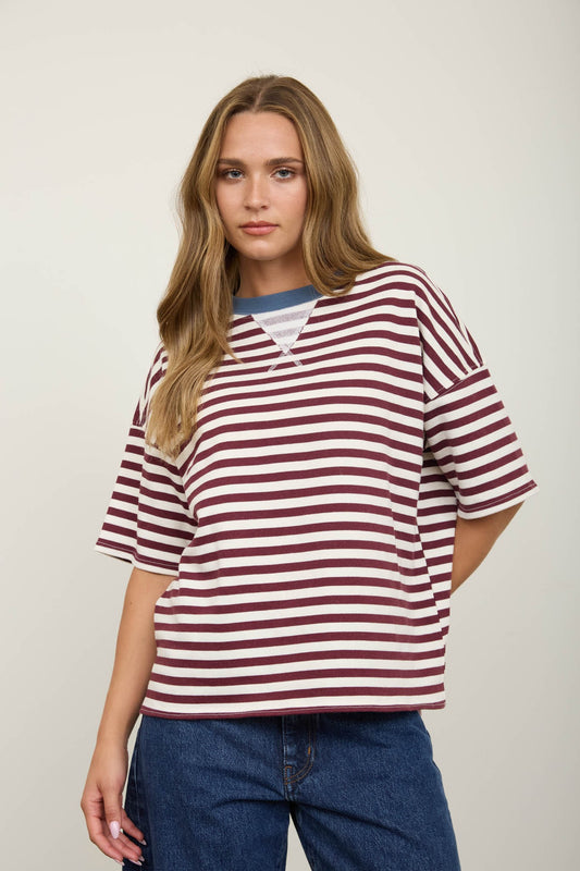 Woman wearing a burgundy striped shirt and jeans against a plain background