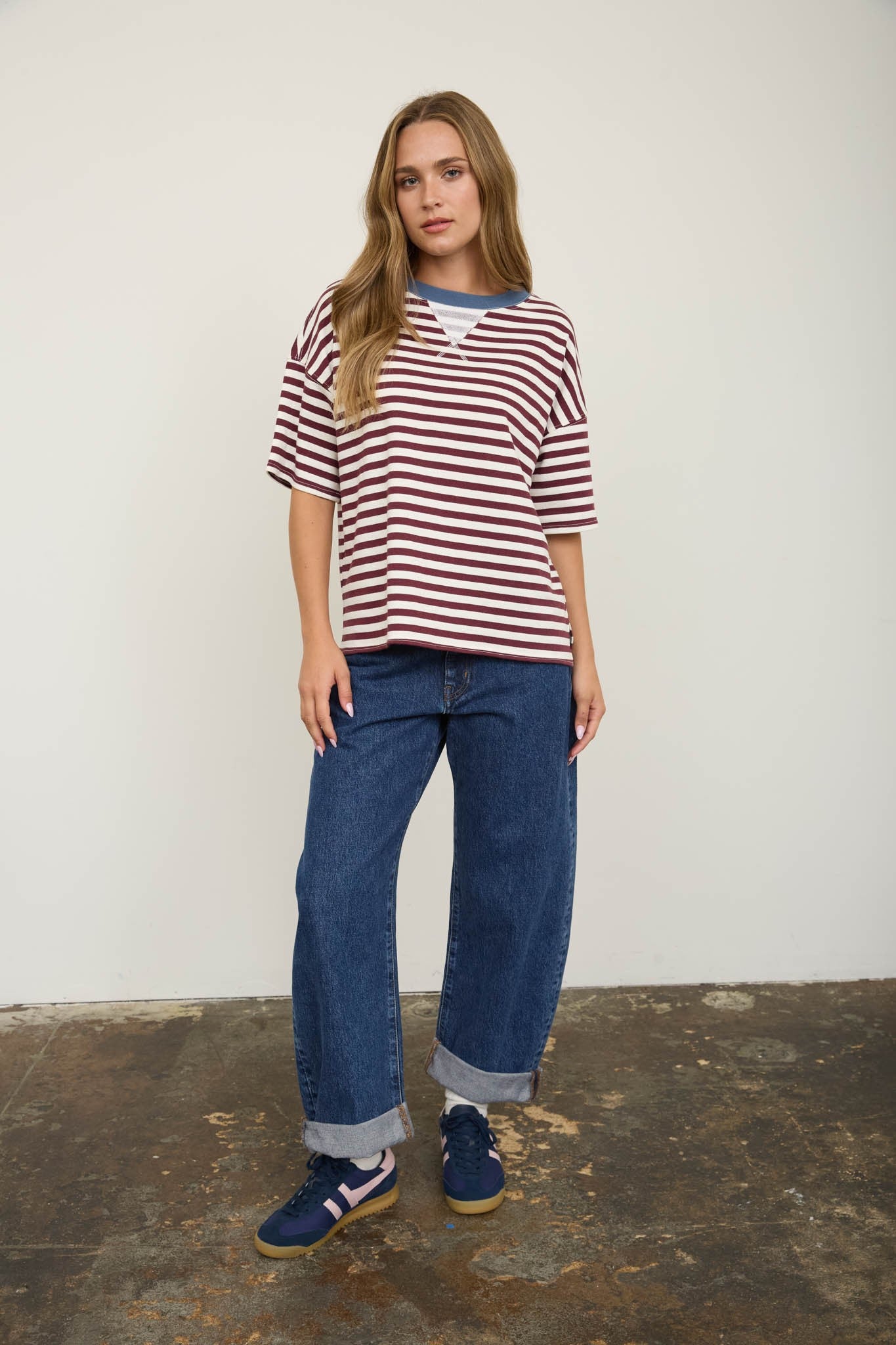Woman wearing a striped shirt and jeans standing against a plain background
