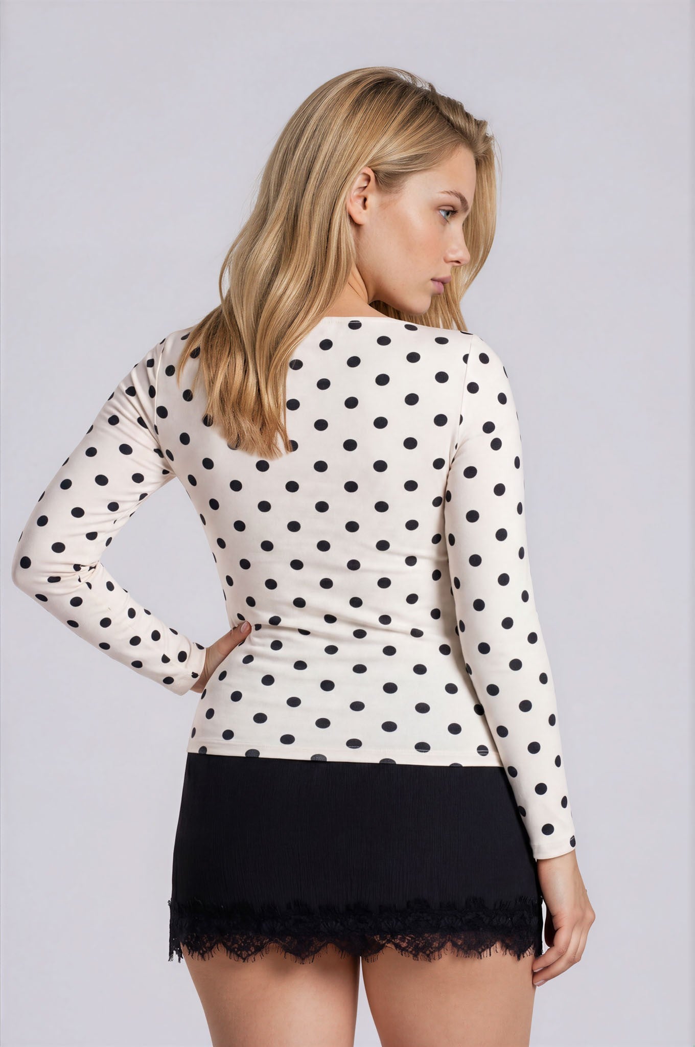 Woman wearing a polka dot top and black skirt against a plain background