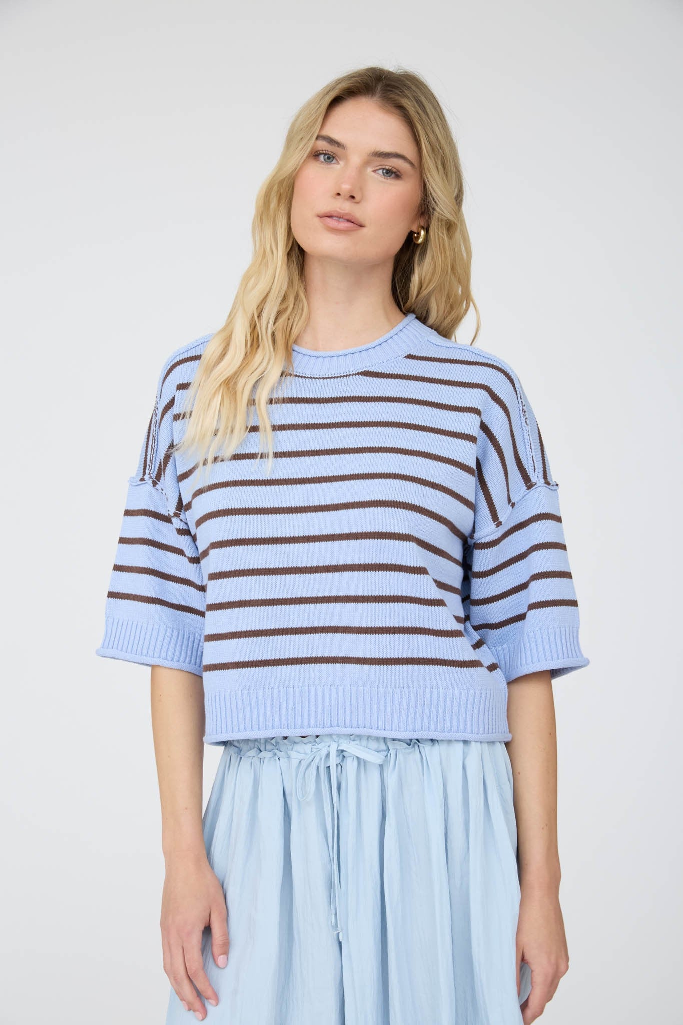 Woman wearing a light blue and brown striped sweater with a plain background