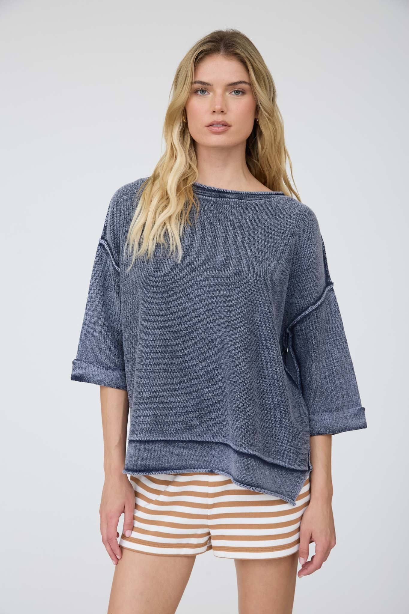 Woman wearing a blue oversized sweater and striped shorts on a white background