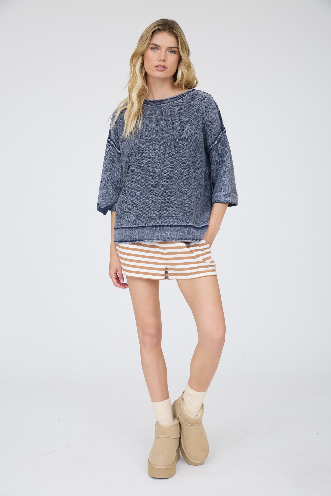Woman wearing a blue sweater, striped shorts, and beige boots on a white background