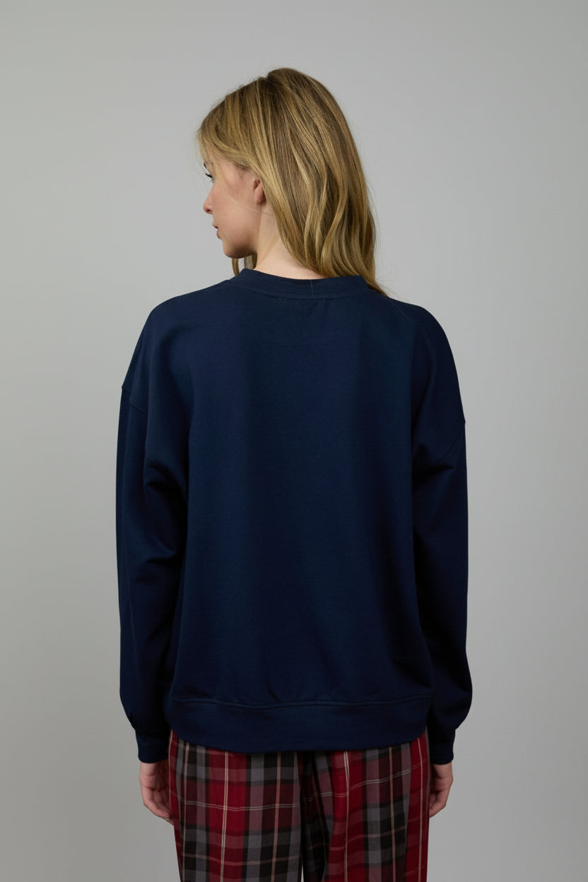 Person wearing a navy blue sweatshirt and plaid pants standing in front of a wooden panel wall.