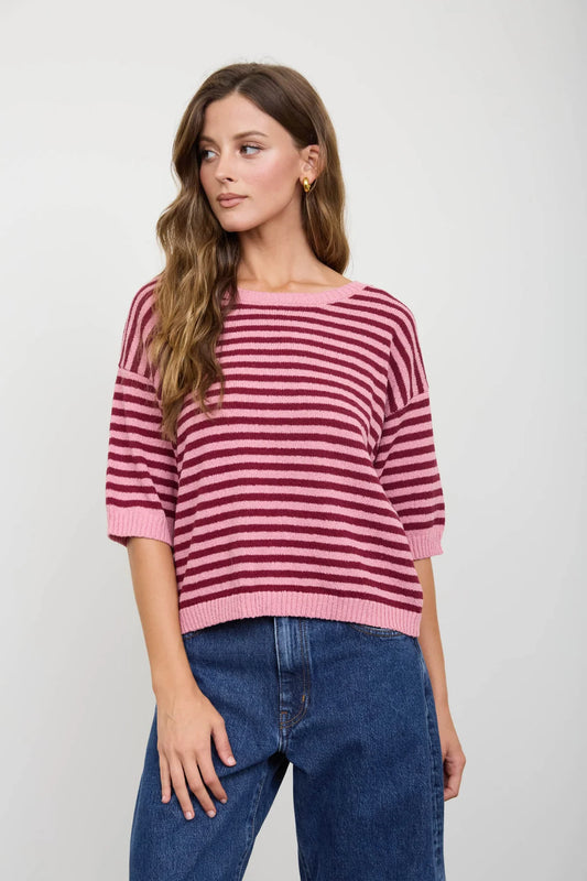 Woman wearing a pink and red striped sweater with blue jeans on a white background
