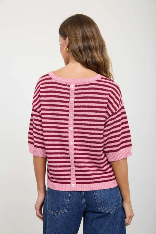 Back view of a woman wearing a pink and red striped sweater with a plain background