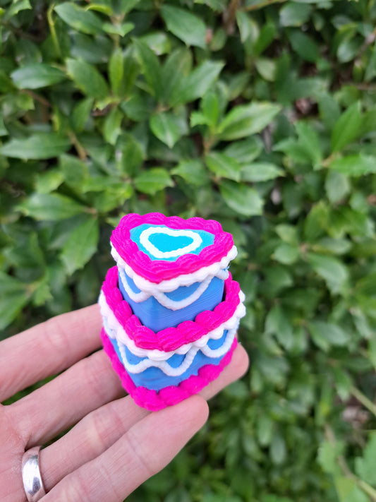 Colorful two-tier plastic cake on a hand with a green leafy background