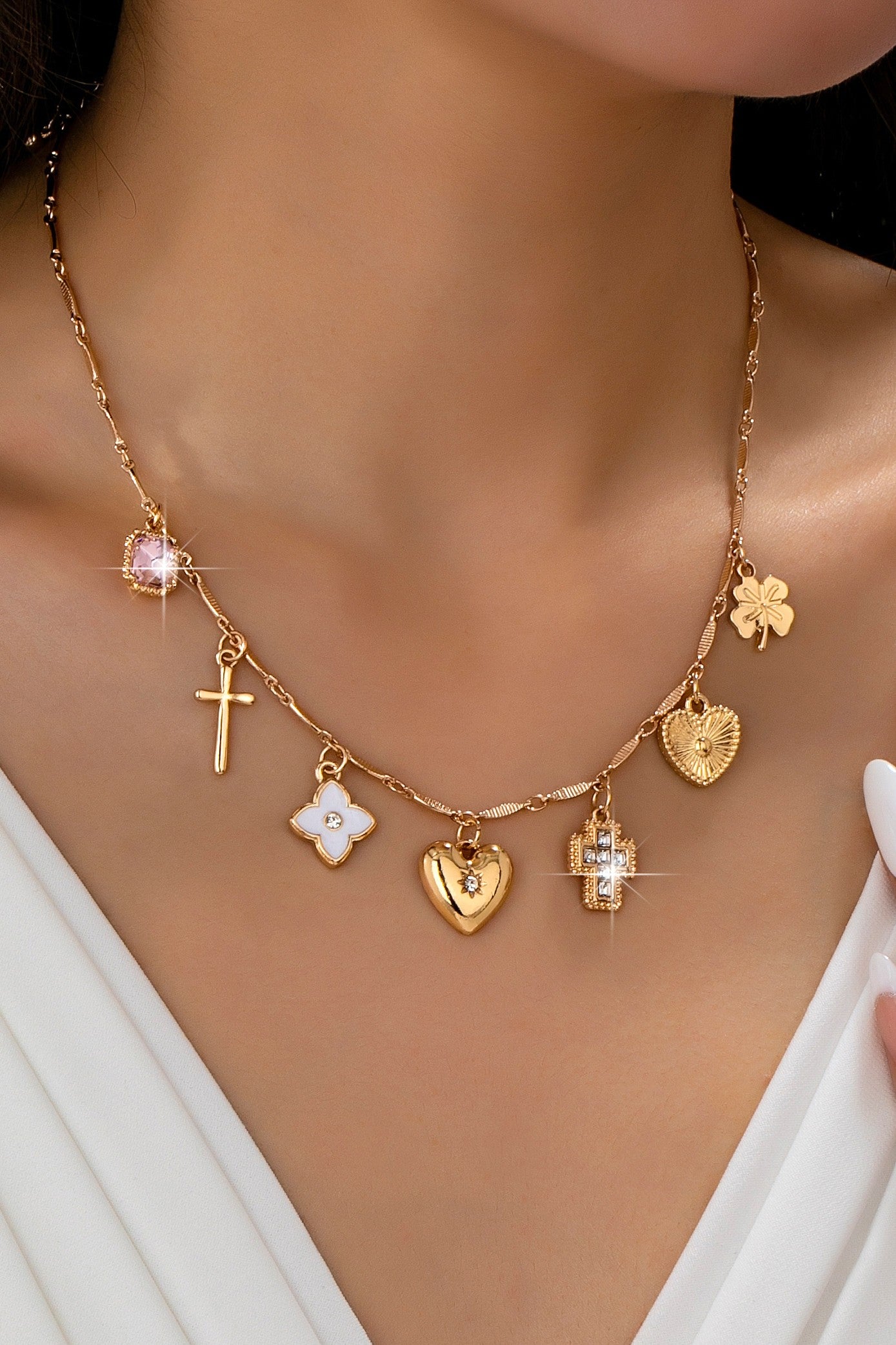Gold necklace with various charms on a person wearing a white top.