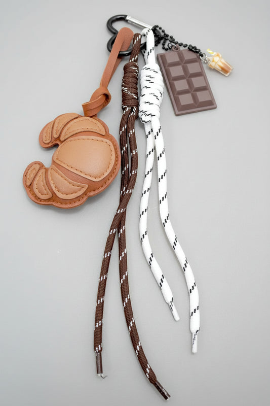 Keychain with brown and white strap, leather charm, and chocolate bar charm on a yellow background