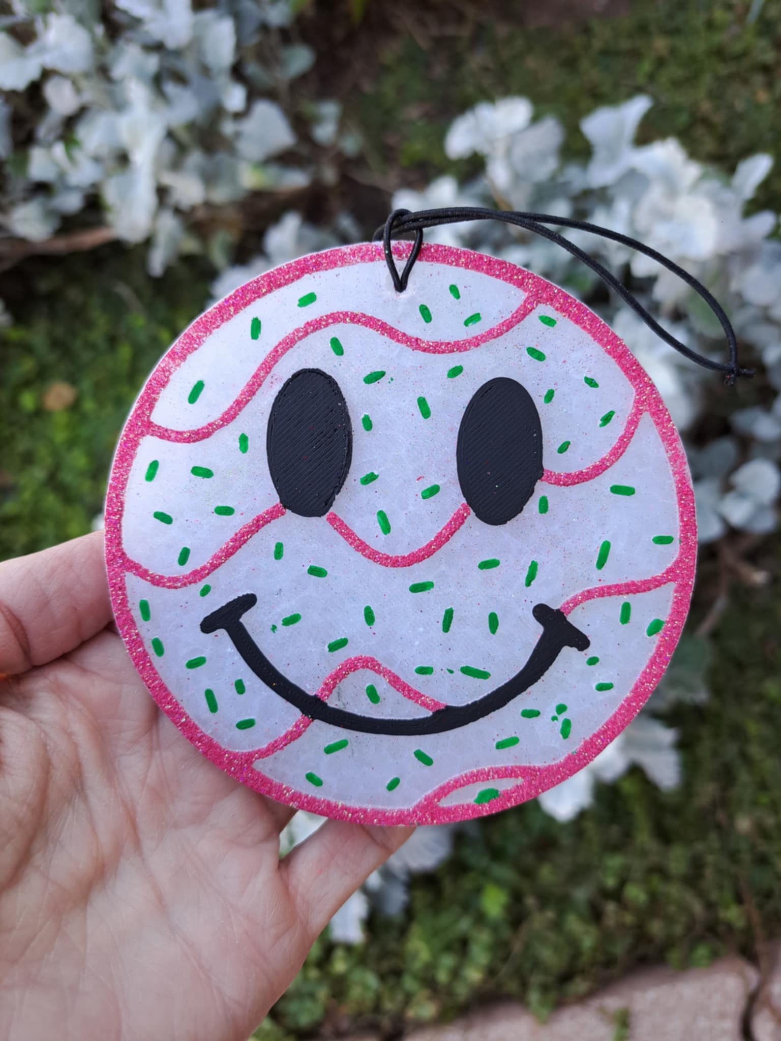 Circular smiley face freshie with pink border held by a hand against a blurred natural background