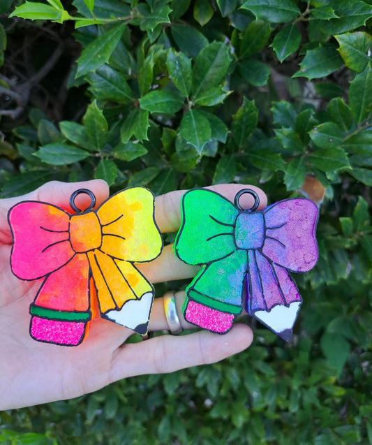 Two colorful bow-shaped freshies held in front of a green leafy background