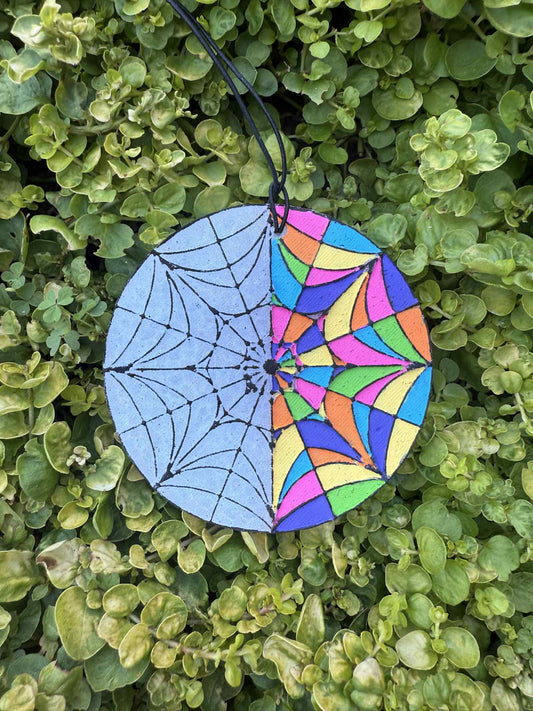 Colorful spider web design on a round blue background hanging on green leaves.