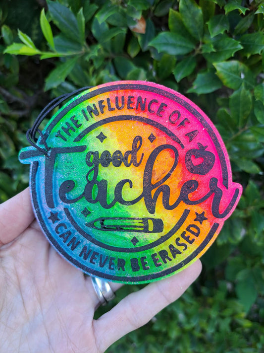 Colorful freshie with black text 'good teacher' held by a hand against a green leafy background