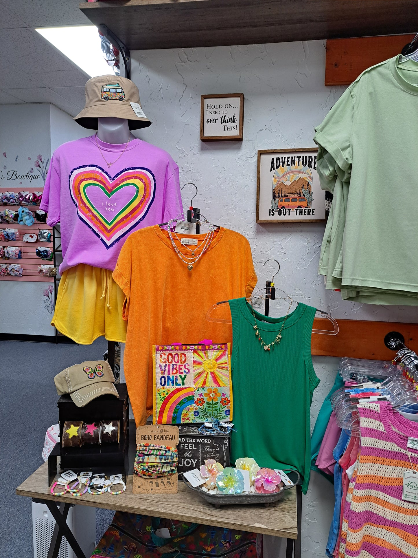 Display of colorful t-shirts and accessories on a table with a white wall background.