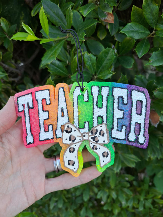 Colorful 'TEACHER' freshie with a leopard bow held against a green leafy background