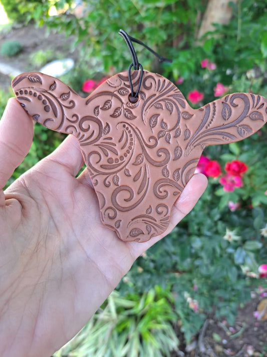 Leather tooled cow head freshie held in front of greenery