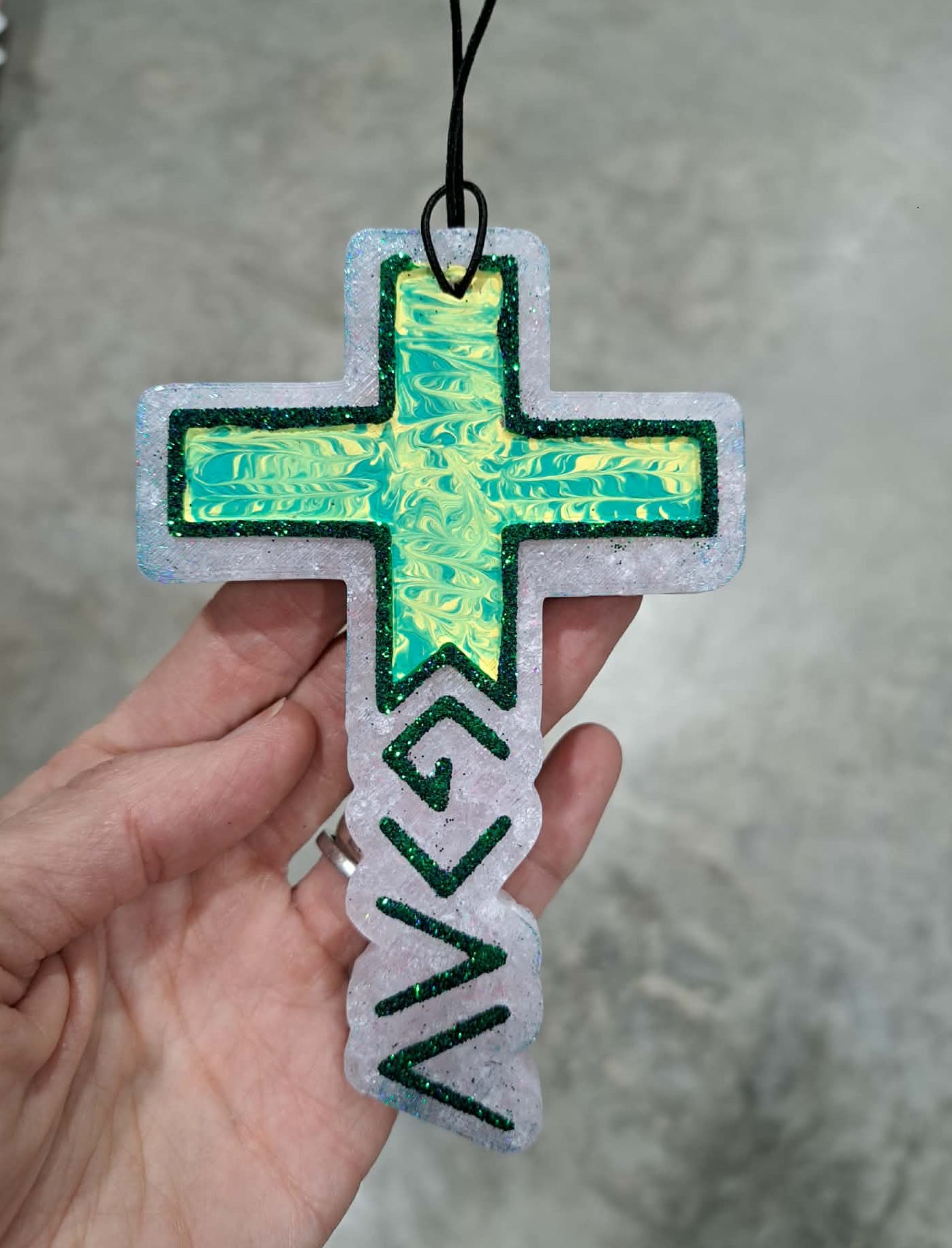Cross-shaped freshie with green and black design held by a hand against a neutral background
