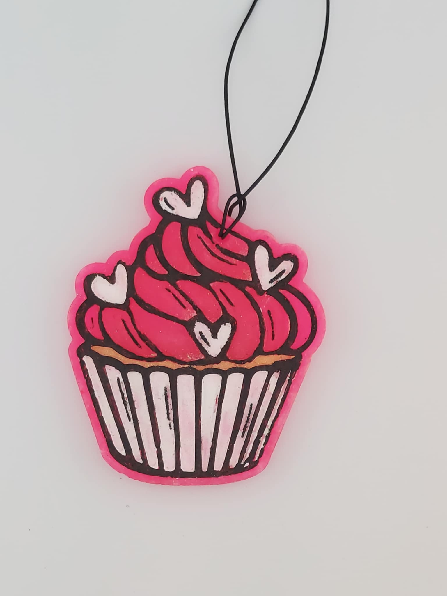 A pink and red heart-shaped air freshener with a cupcake design and strings for hanging.