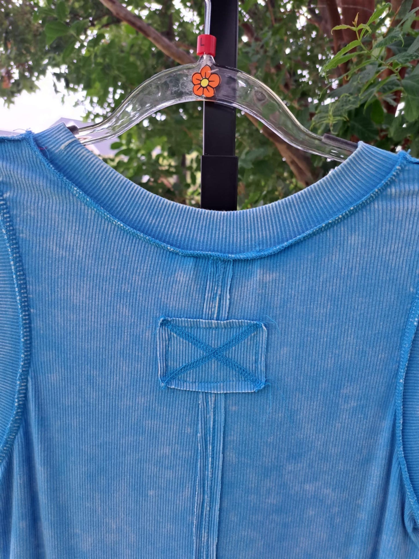 Blue shirt on a hanger with a floral tag against a blurred green background