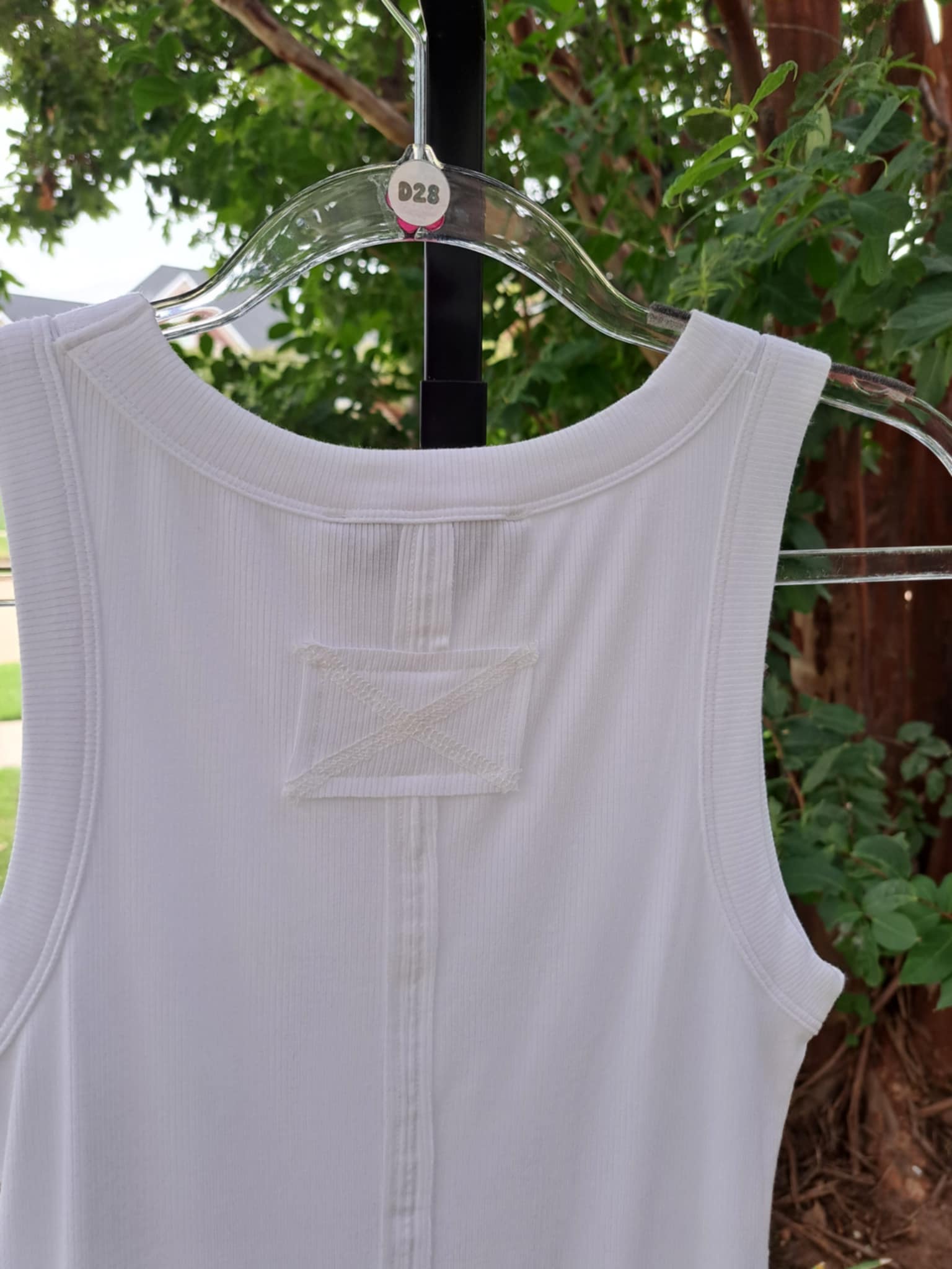 close up of the back of a white ribbed tank top with greenery in background