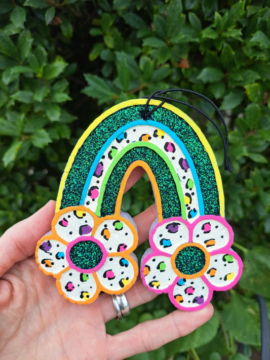 Colorful rainbow air freshener held in a hand with a green leafy background