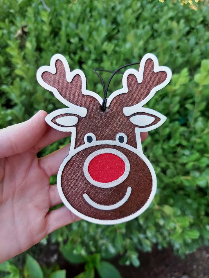 Hand holding a reindeer-shaped freshie with a red nose against a green leafy background