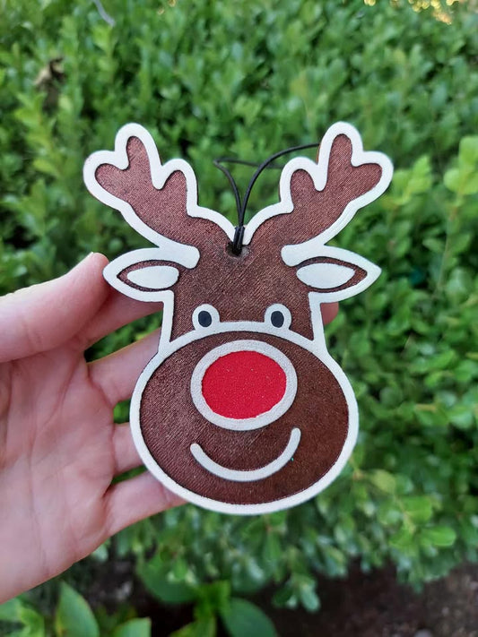 Hand holding a reindeer-shaped freshie with a red nose against a green leafy background